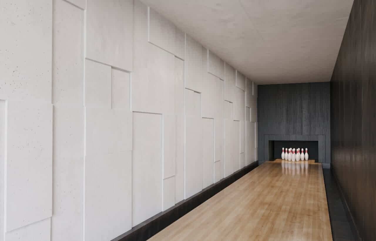 The pale-wood bowling lane, between a wall of irregular concrete panels and a plane of dark timber.